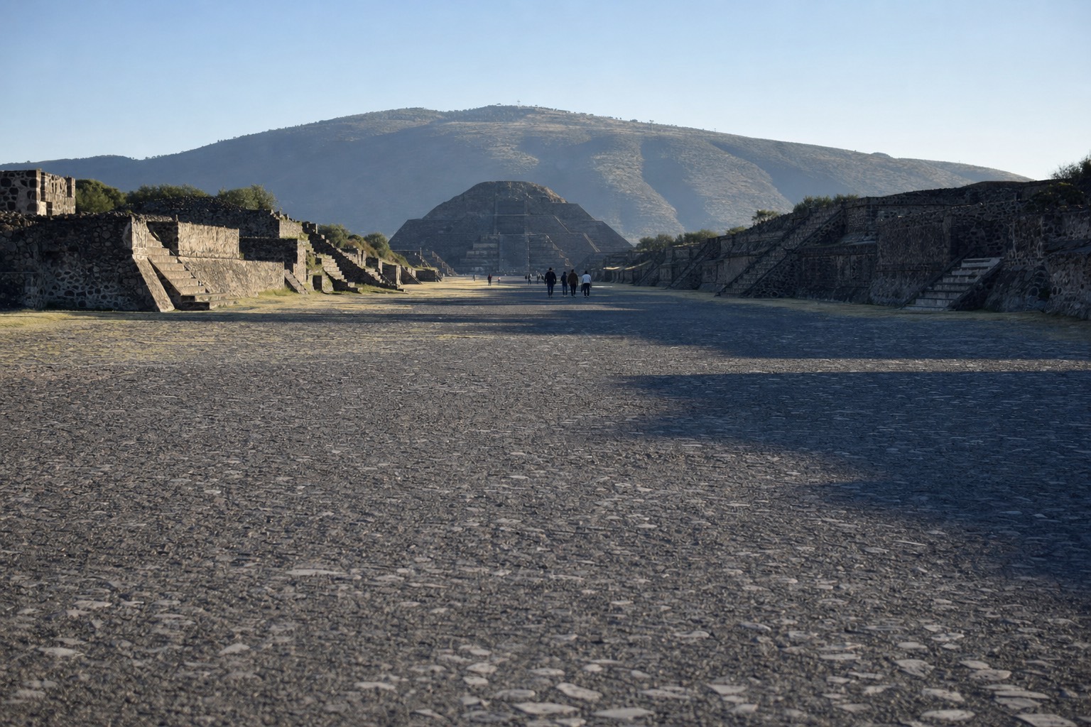 Visitors walking the Avenue of the Dead at Teotihuacan with the Pyramid of the Moon ahead in morning light