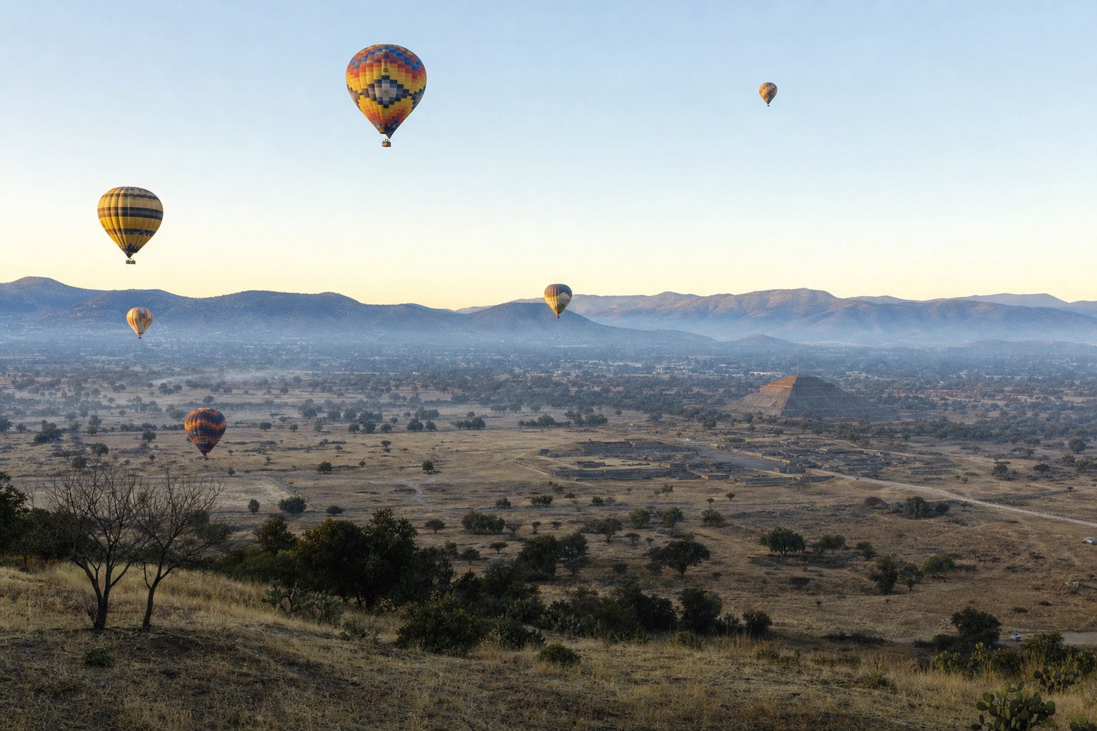 Balloons rising over the Teotihuacan valley at first light with Mexico City's mountains on the horizon