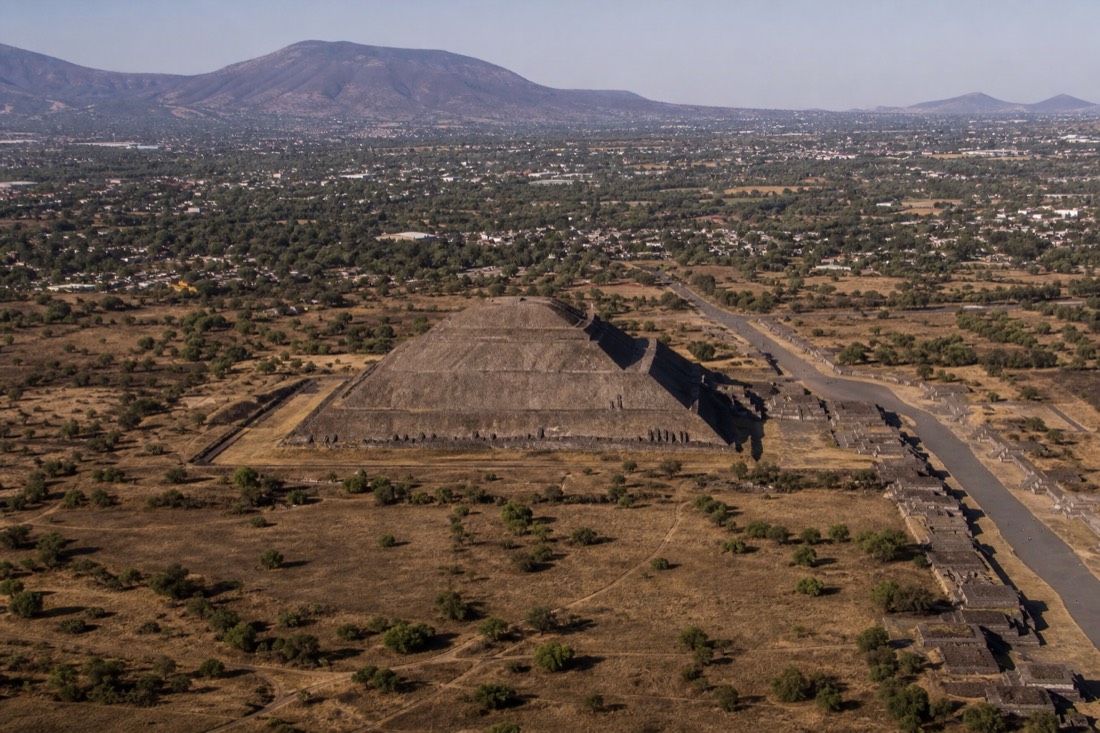 A stepped pyramid at middle distance from the air, its terraces edged with shadow