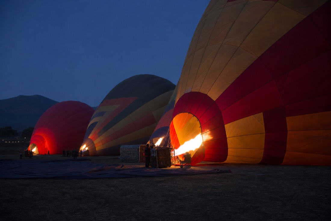 Hot air balloon envelopes inflating on a dark launch field near Teotihuacan before sunrise