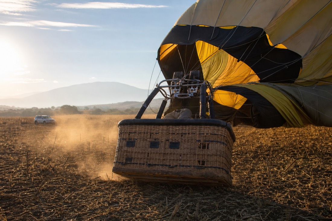 A hot air balloon basket touching down in a dry field with the envelope collapsing behind it